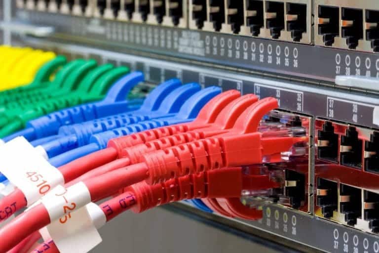 A close-up of colourful, labelled ethernet cables (red, blue, green) plugged into a network patch panel.
