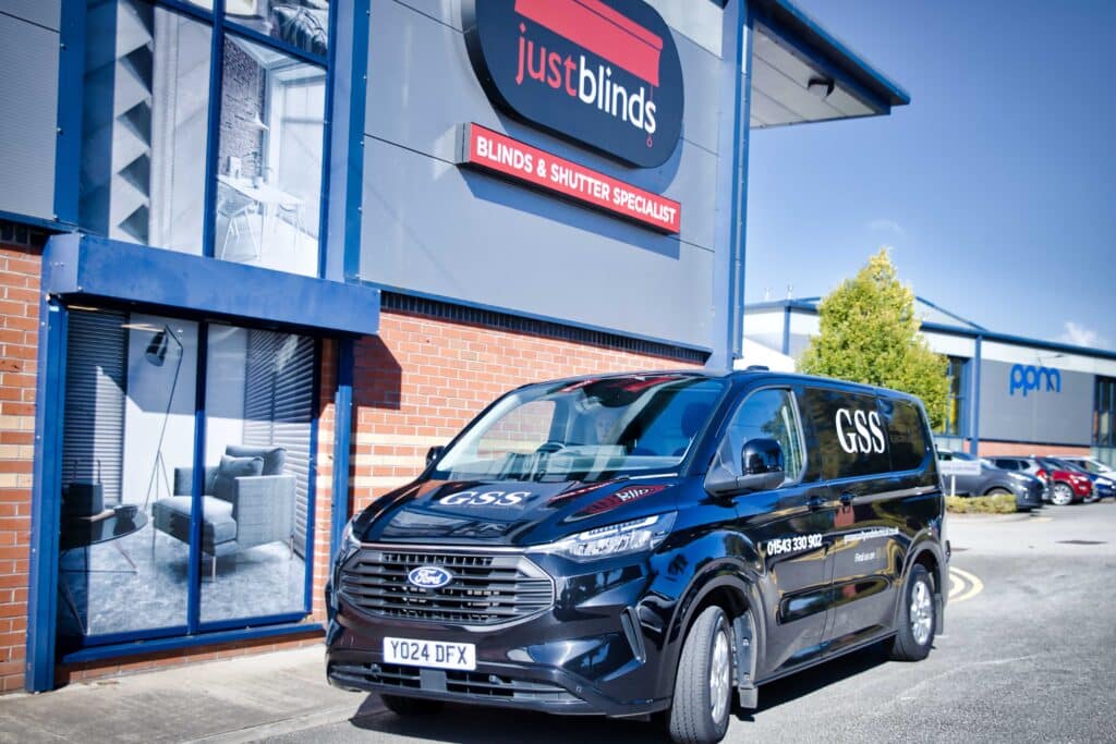 A black GSS Security & Electrical van parked outside the Just Blinds showroom in a commercial business park.