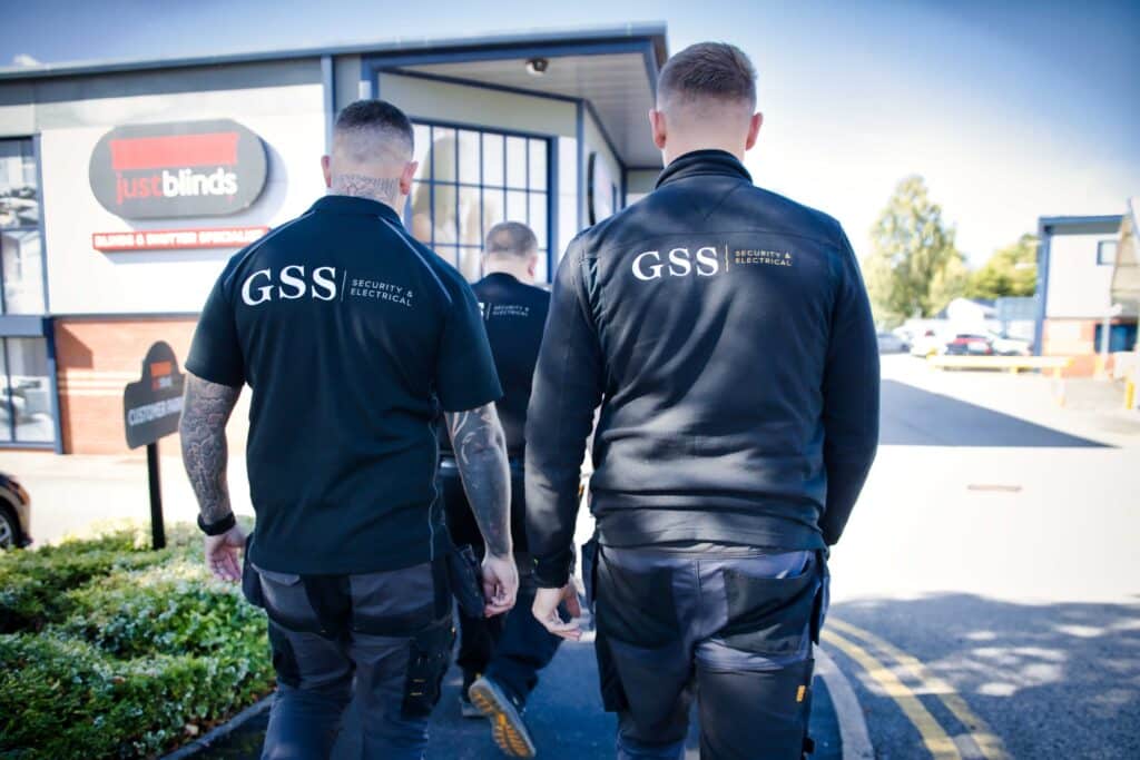 hree GSS Security & Electrical engineers walking away from the camera towards a client premises, wearing branded black uniforms and work trousers.