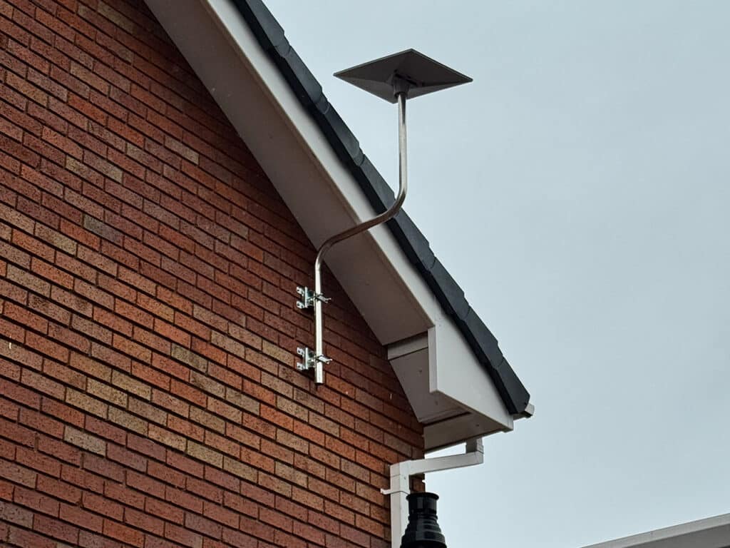 A rectangular Starlink satellite dish professionally mounted on a metal mast bracketed to a red brick wall, positioned above the roofline to ensure optimal signal reception for high-speed internet.